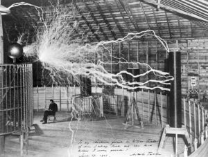 Tesla sentado em seu laboratório e afrente sua bobina com raios